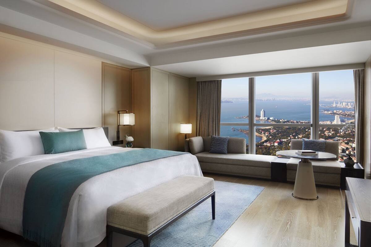 A hotel room with a large bed, a sofa, a small table, and a view of the city.