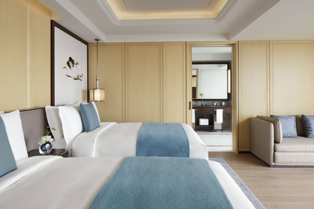 A hotel room with two beds, a sofa, a desk, and a bathroom visible through an open door.