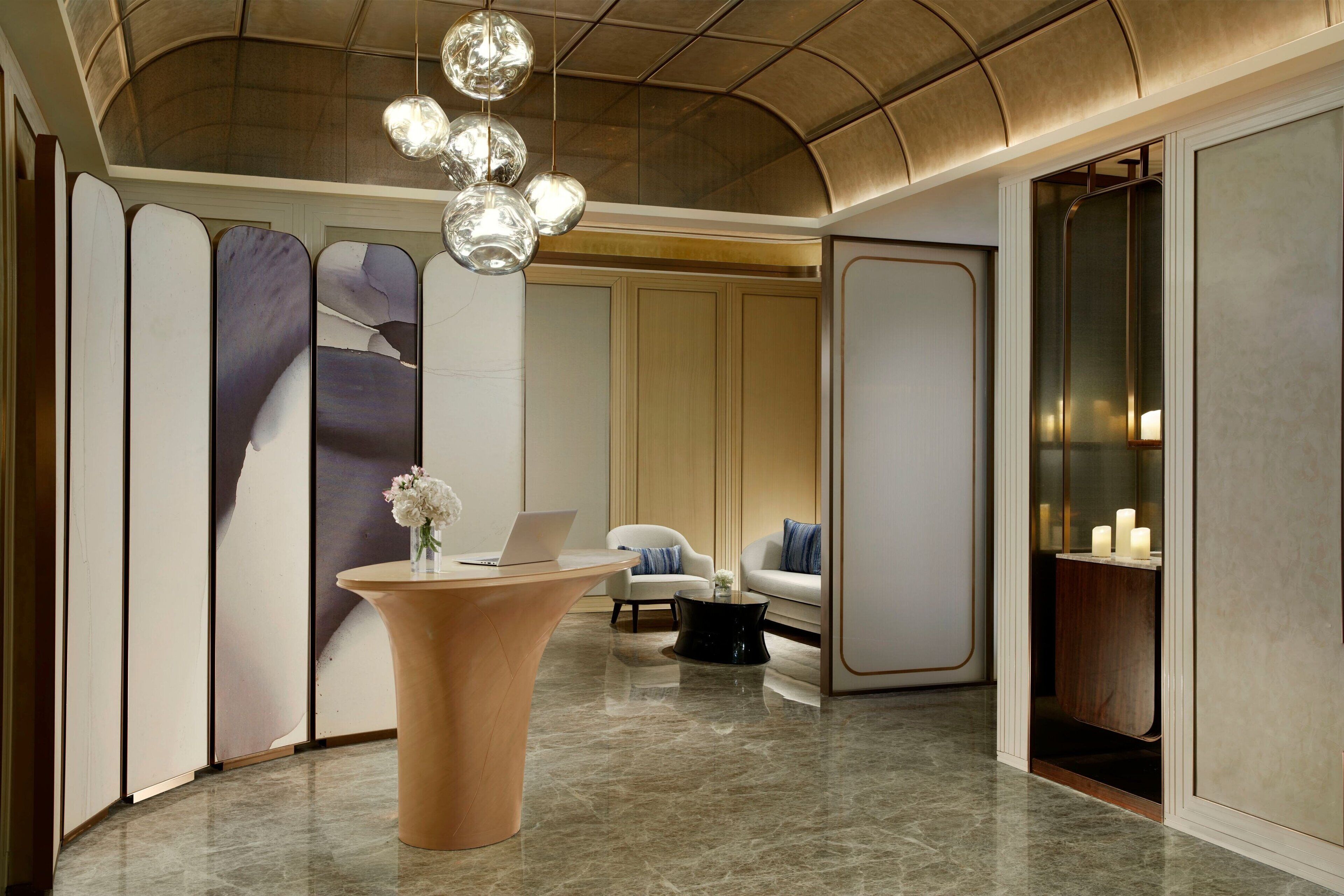 A modern lobby with a curved ceiling, a reception desk, a seating area with a sofa and chairs, and a decorative wall with abstract panels.
