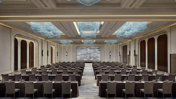 A conference room with rows of tables and chairs, a patterned carpet, and a large chandelier.