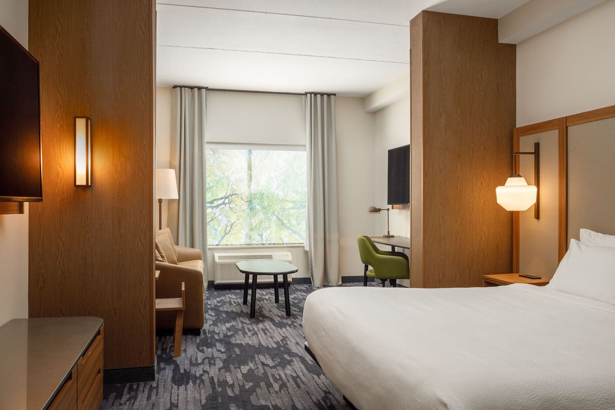 Une chambre d’hôtel avec un lit, un bureau, une chaise, une télévision et une fenêtre avec des rideaux.