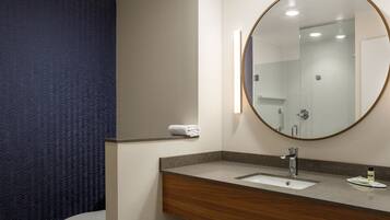 Un baño moderno con tocador de madera, un espejo redondo y un lavamanos blanco.