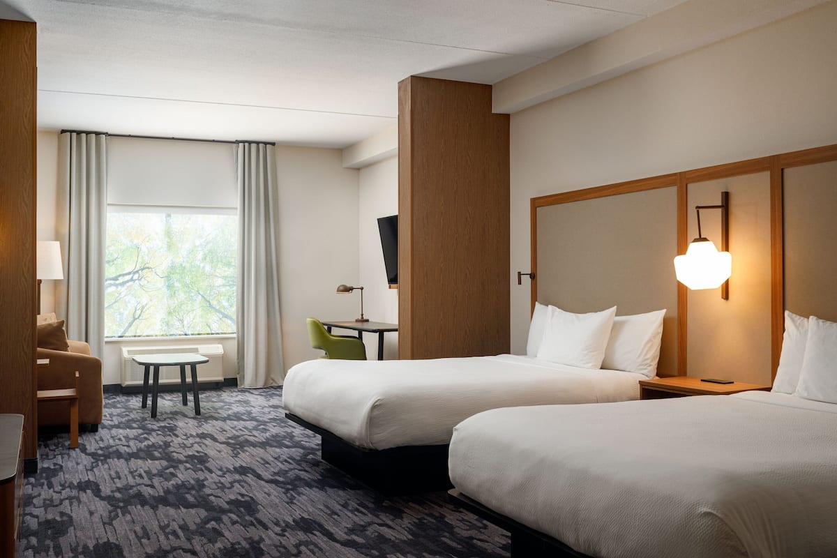 Une chambre d’hôtel avec deux lits, un bureau, une chaise et une fenêtre avec des rideaux.