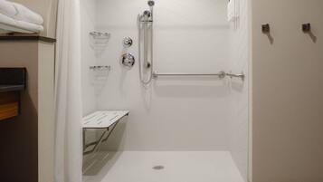 A walk-in shower with a white tiled wall, a showerhead, a handrail, and a towel rack.