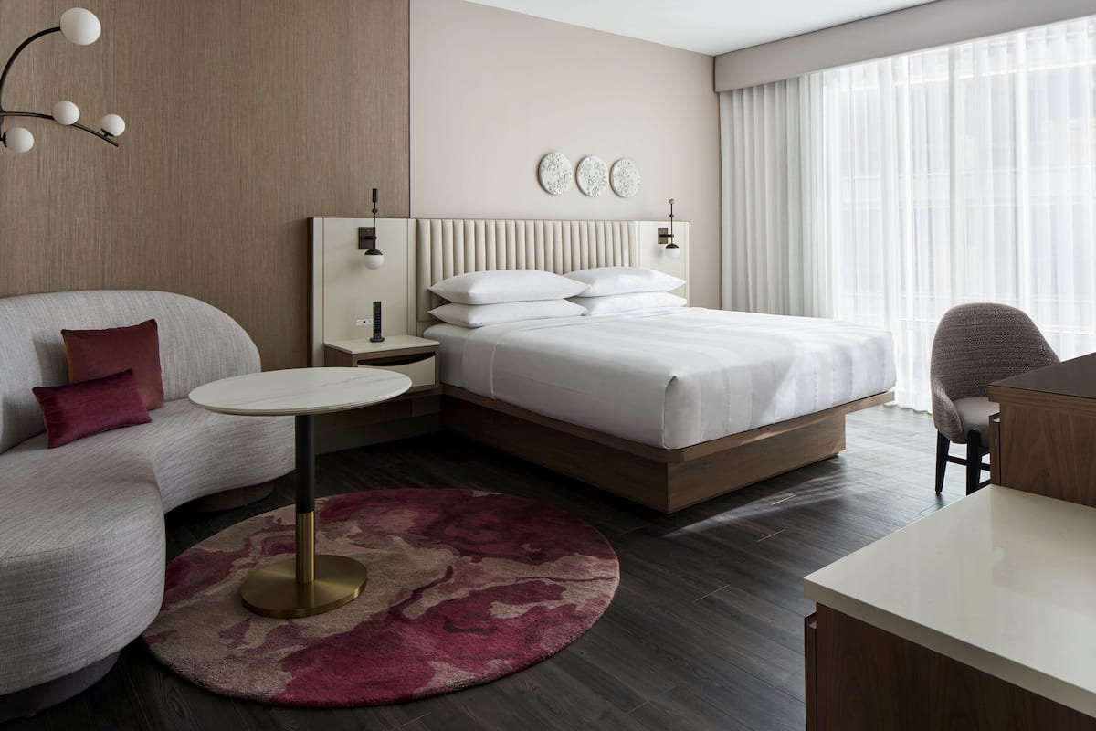 Een moderne hotelkamer met een gebogen bank, een ronde salontafel, een bed met hoofdeinde, een nachtkastje en een bureau.