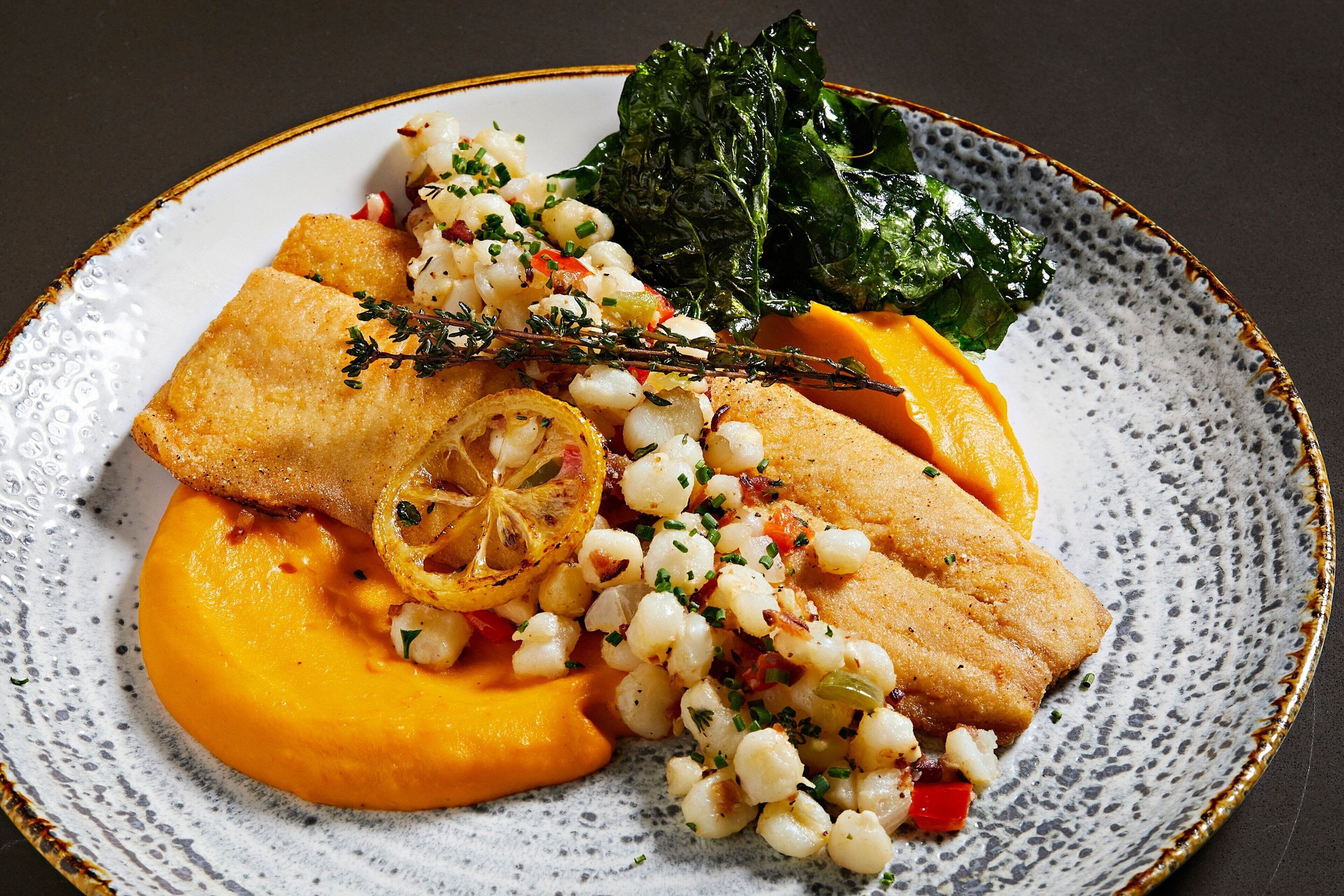 Une assiette de nourriture contenant du poisson, du maïs et des légumes verts.