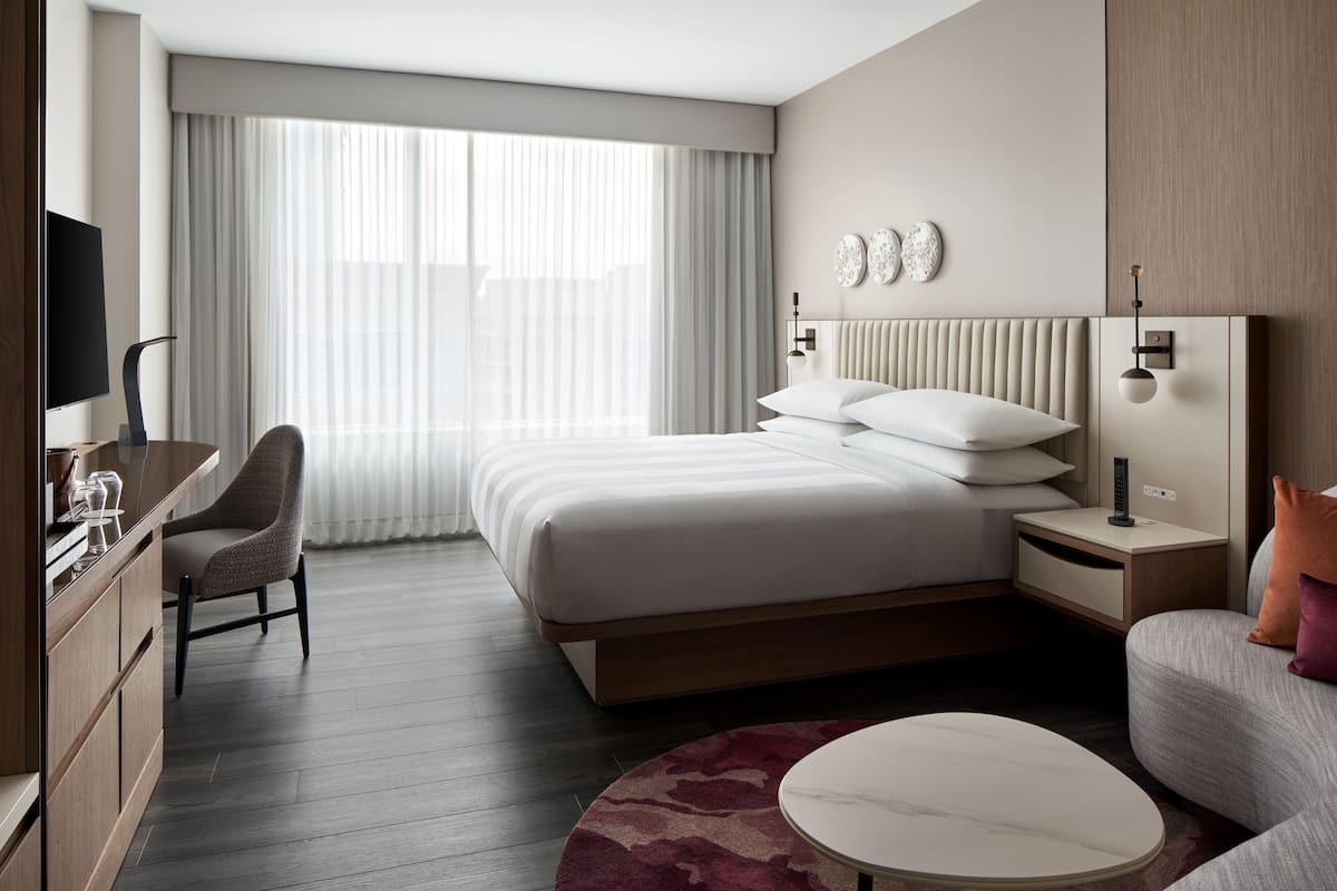 Een moderne hotelkamer met een groot bed, een bureau met stoel, een televisie en een nachtkastje met lamp.