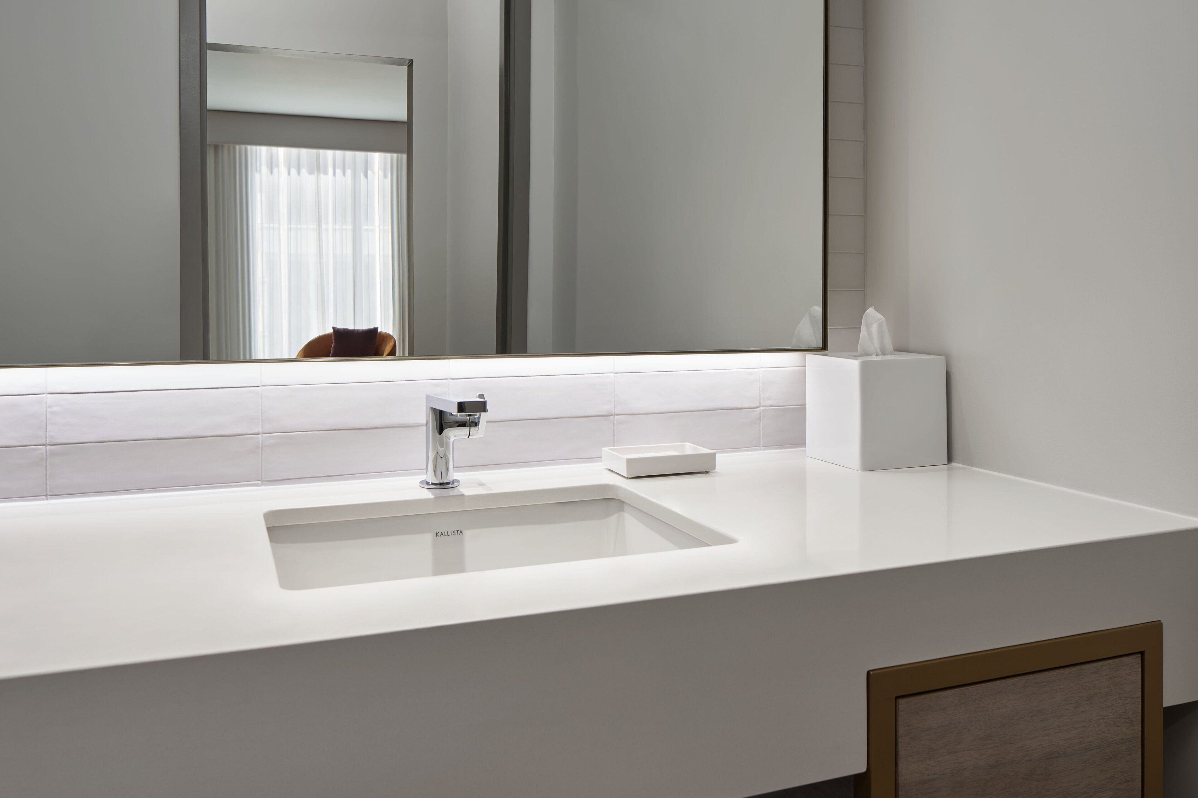 Une salle de bain moderne avec un lavabo blanc, un miroir et une fenêtre avec des rideaux.