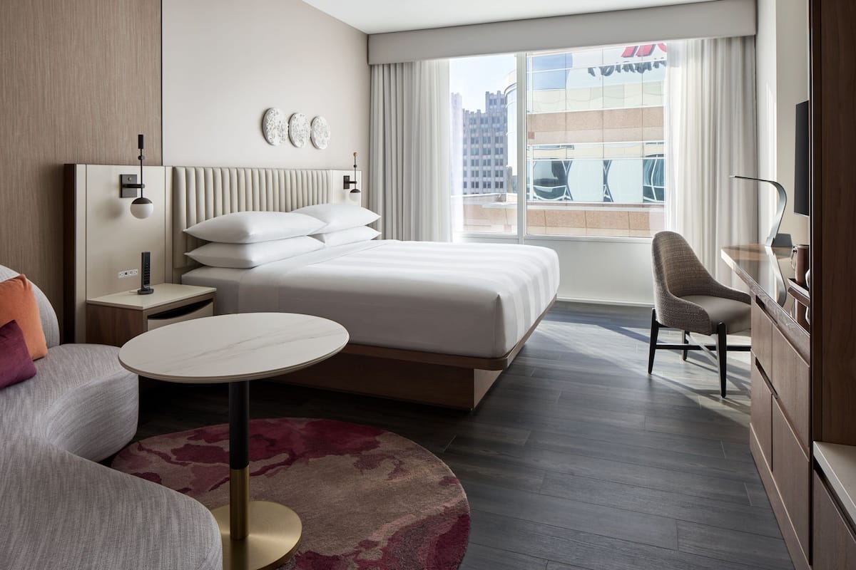 Een moderne hotelkamer met een groot bed, een ronde salontafel, een bank, een bureau en uitzicht op de stad.