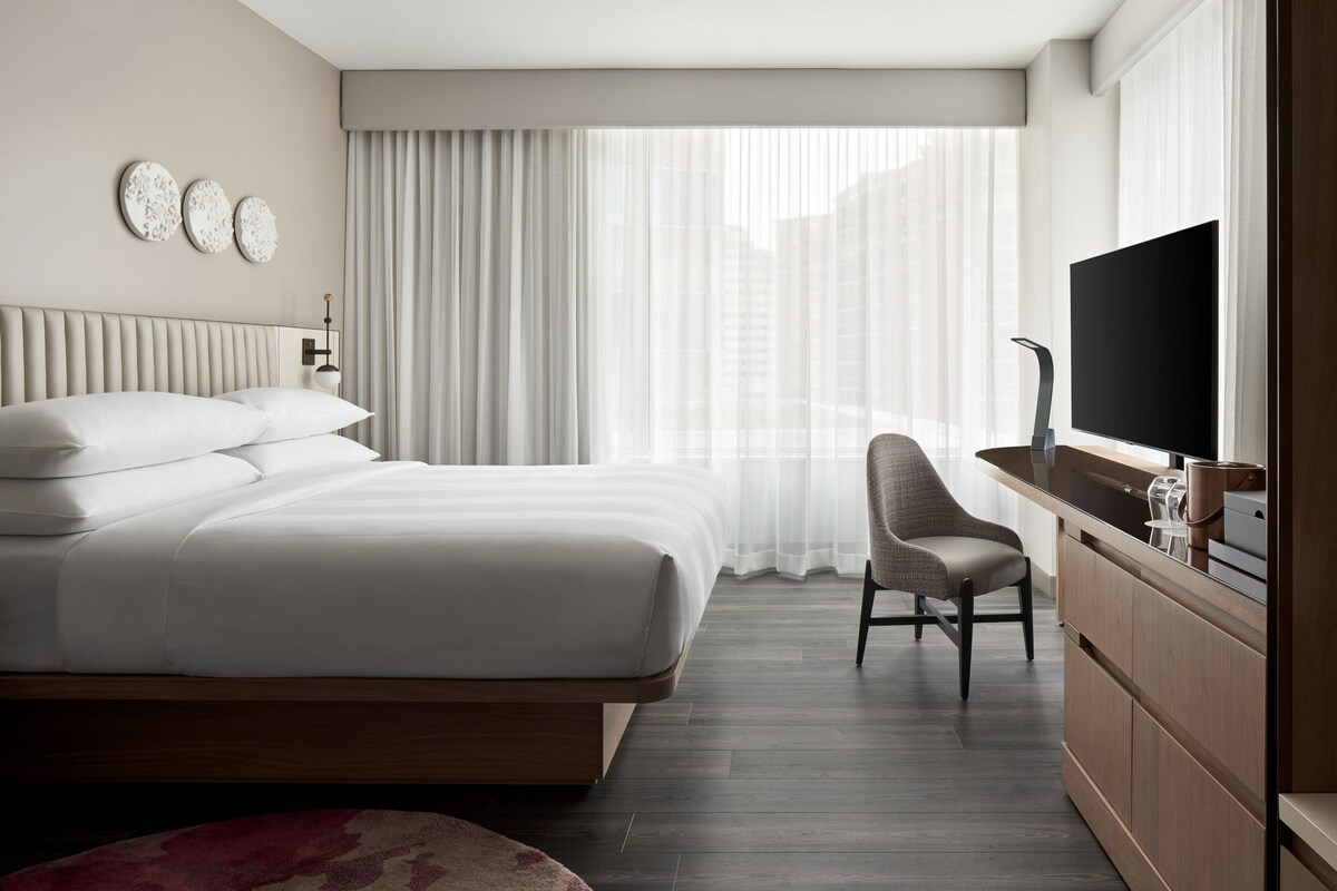 Une chambre d’hôtel avec un grand lit, un bureau avec une chaise, une télévision et une fenêtre avec des rideaux.