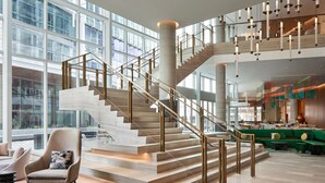 A spacious lobby with a central staircase, large windows, and a seating area with modern furniture.