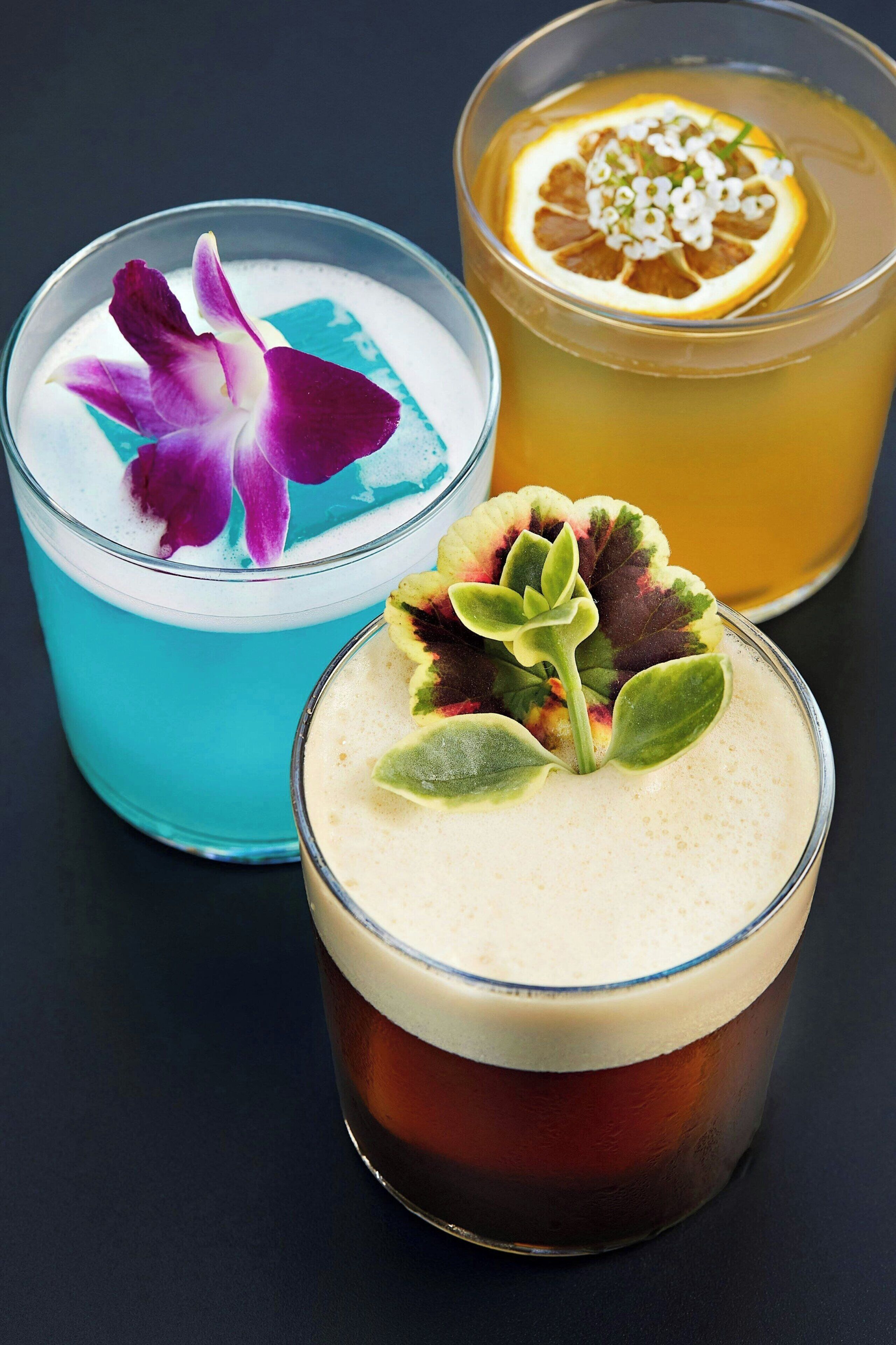 Three glasses of different beverages, each with unique garnishes.