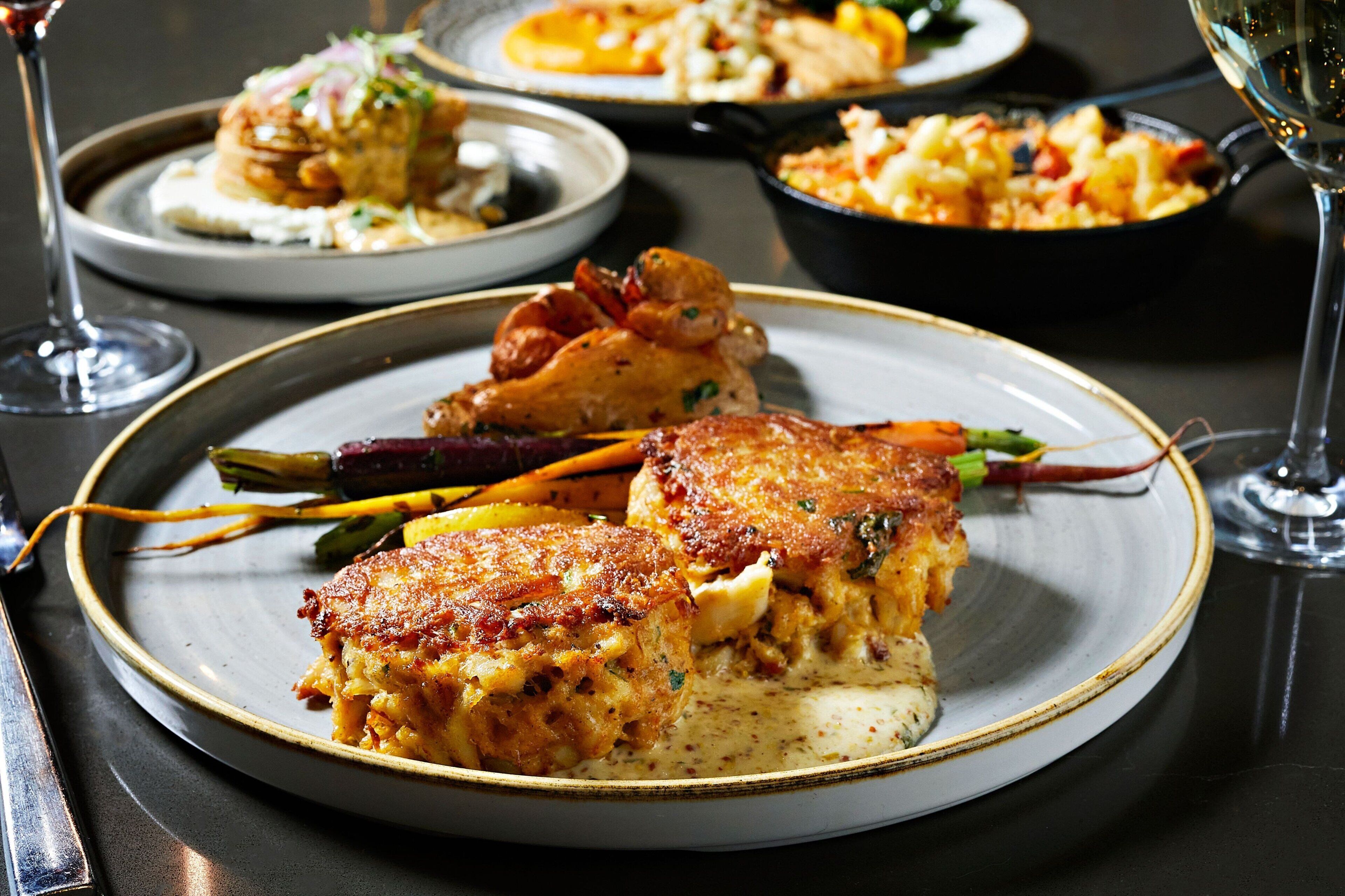 A dining table with plates of food, glasses of wine, and a fork.