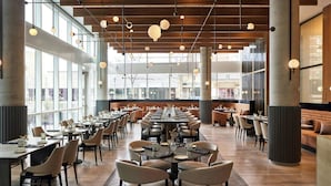 Een ruime eetzaal met hoge plafonds, hangende吊灯, en grote ramen met uitzicht op buiten. Tafels zijn netjes gerangschikt met stoelen, en de vloer is van gepolijst hout.