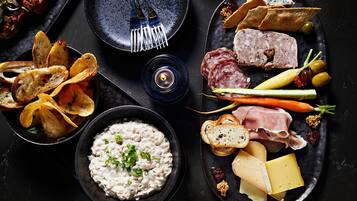 Variedad de alimentos, como papas fritas, queso, carnes, aceitunas y un bol de salsa, dispuestas sobre un plato oscuro.