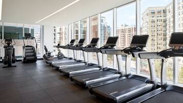 A gym with treadmills aligned in a row, a rowing machine, and a weight bench.