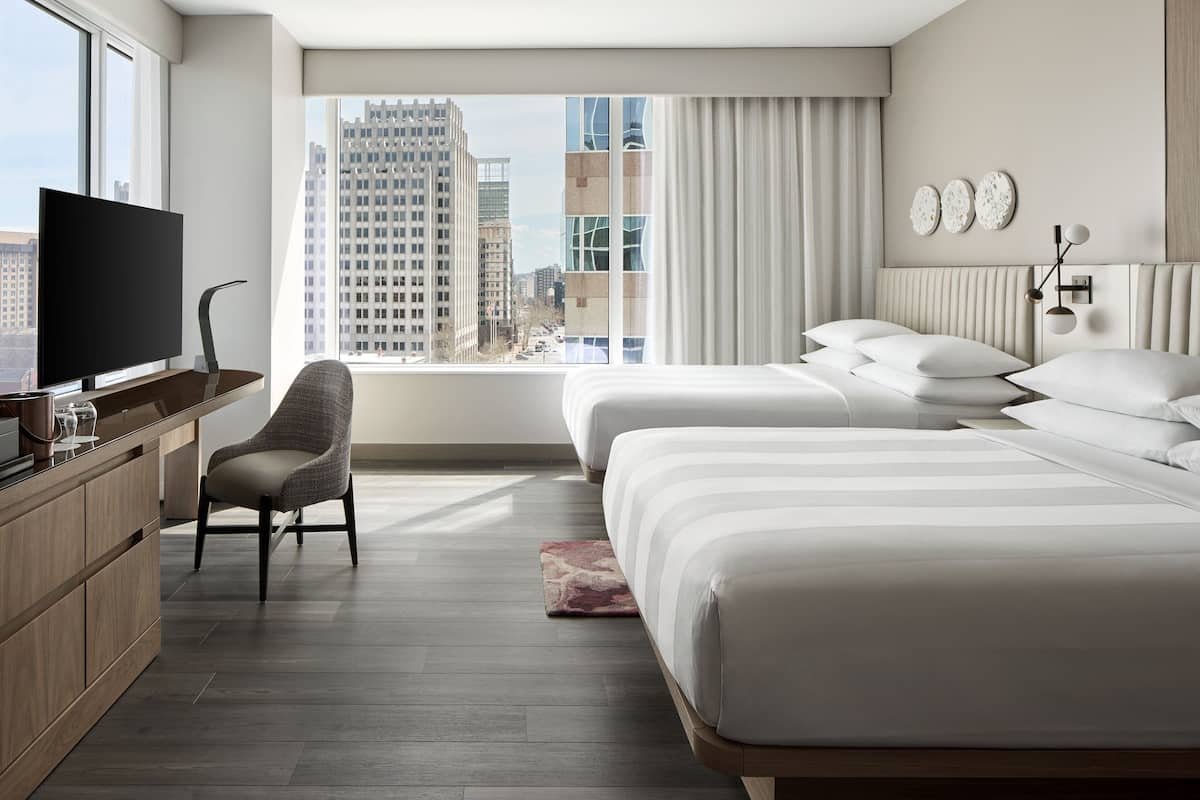Een moderne hotelkamer met een groot raam, twee bedden, een televisie, een bureau en een stoel.
