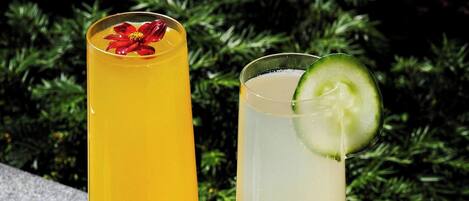 Dos vasos altos de bebidas sobre una superficie de piedra con follaje de fondo.
