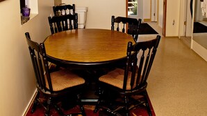 A dining area with a round wooden table surrounded by chairs, a television mounted on the wall, and a wooden ceiling beam. - Cozy, quirky and quaint updated Farm House surrounded by Sleeping Bear Dunes. (Maple City)