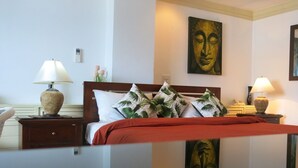 Une chambre d’hôtel comprenant un lit, deux tables de chevet, une petite table, un miroir fixé au mur et un tableau au-dessus du lit.