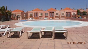 A swimming pool area with lounge chairs and a building with multiple windows and a red roof. - Spacious 3 bed/2 bath house, on a gated complex, Fibre Wifi. Two communal pools. (Antigua)