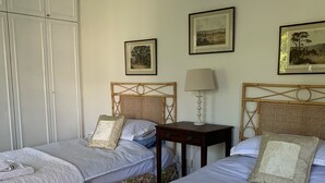 A hotel room with two single beds, a nightstand, a lamp, and a wardrobe.