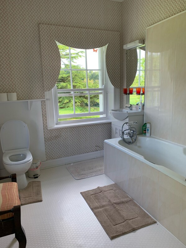 A bathroom with a toilet, sink, bathtub, and a window with a view of greenery.
