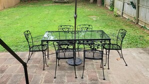 A patio with a table and chairs, a blue umbrella, and a wooden fence in the background. - Steps to the Beach, Cozy Year Round Cottage 🐾 Pet Friendly (Old Saybrook)