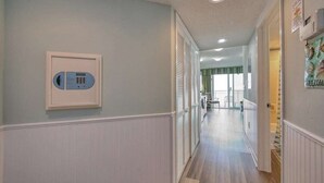 Um corredor com telefone, uma porta e vista para outro quarto.