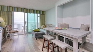 Uma sala de estar moderna com área de jantar, janelas amplas e vista para o mar.