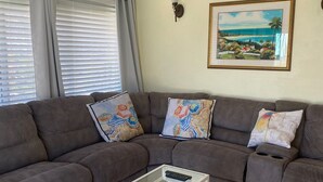 Ein Wohnzimmer mit einem braunen Ecksofa, einem Glastisch und einem gerahmten Landschaftsbild an der Wand.