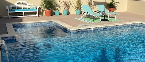 Relax by the serene pool surrounded by lush greenery and a comfortable bench.