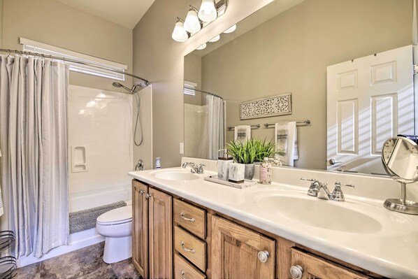 A bathroom with a double sink, wooden cabinets, a shower, and a large mirror. - Goodyear Home w/ Pool: Near Golf & Ballpark! (Goodyear)