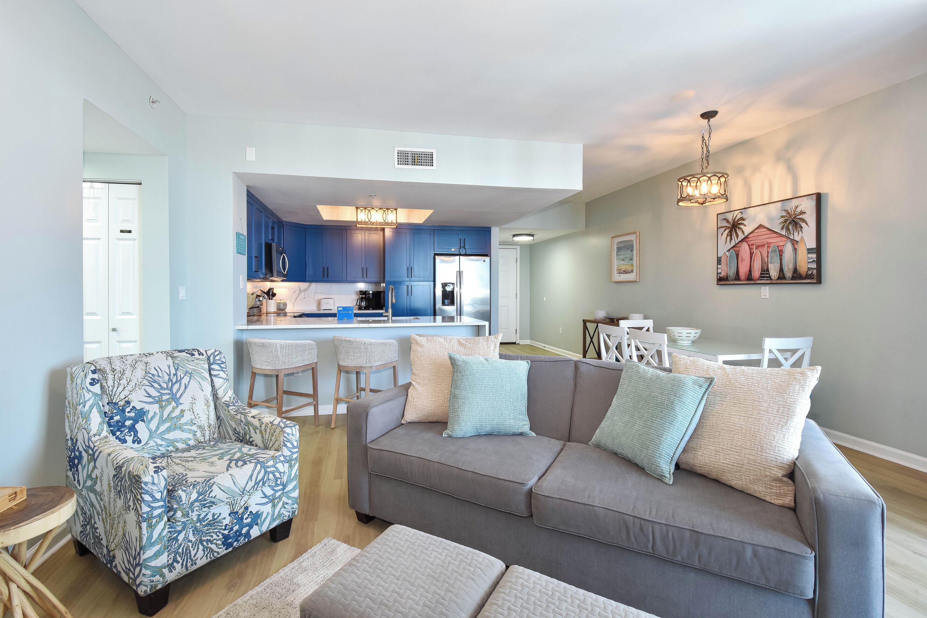 A living room with a grey sofa, blue armchair, and a dining area with white chairs.