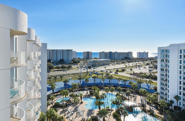 A resort with a large pool area, multiple balconies, and a view of the surrounding cityscape.