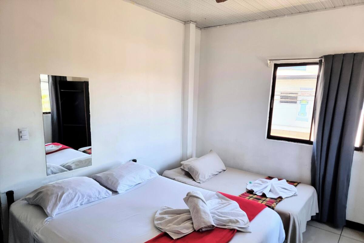 A hotel room with two beds, a window with curtains, a mirror, and a red towel on the bed.