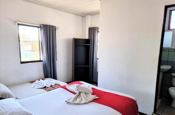 A hotel room with two beds, a window with curtains, a wardrobe, and a bathroom visible through an open door. - Hotel el Descanso (San José)