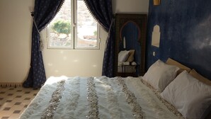 Una camera da letto con un letto, una finestra con tende, una sedia e un elemento fissato al muro.