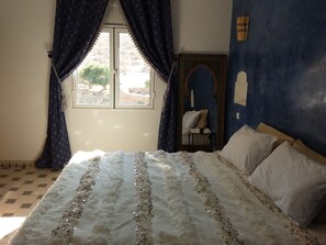 Relax in this serene bedroom with a large bed, window, chair, and shelf.
