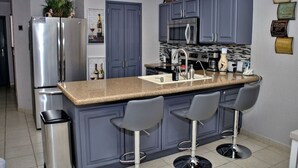 A modern kitchen with grey cabinets, a stainless steel refrigerator, a built-in microwave, and a granite countertop.
