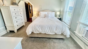 Une chambre à coucher comprenant un lit, une commode, des tables de chevet et une fenêtre avec des stores.