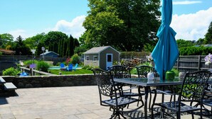 Een terras buiten met een tafel, stoelen, een blauwe parasol en een stenen muur.