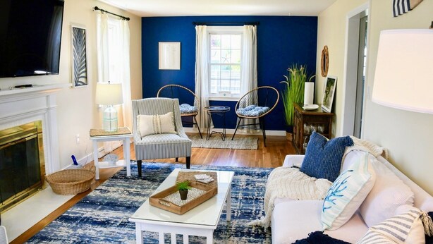 Een woonkamer met een open haard, een televisie, een blauwe accentmuur en een gezellige zithoek met een bank en fauteuils.