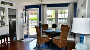 Een eetgedeelte met rieten stoelen, een ronde tafel en een blauwe tafellamp.