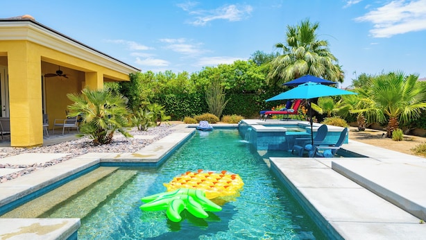 A swimming pool with clear water, surrounded by palm trees and a covered seating area. - Villa Serene Luxurious Resort Vacation Home - pool (Indio)