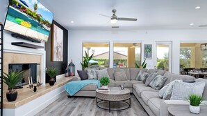 A modern living room with a sectional sofa, a round coffee table, a flat-screen TV mounted on the wall, and a fireplace. - Villa Serene Luxurious Resort Vacation Home - pool (Indio)