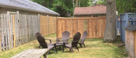 A backyard with a wooden deck, a picnic table, and four Adirondack chairs.