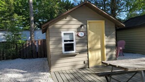 Une petite cabane en bois avec une porte jaune, une fenêtre et une plaque portant le numéro « 5 ».