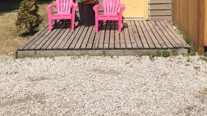 Une petite cabane en bois avec une porte jaune, deux fauteuils Adirondack roses et un petit jardin.