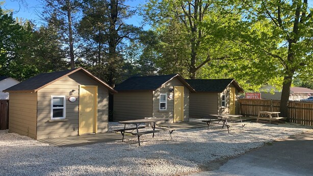 Une rangée de petits chalets à un seul étage, avec une allée en gravier et des tables de pique-nique devant.